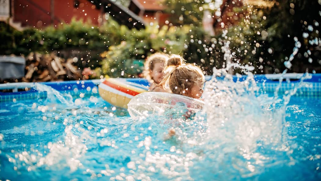 So geht Ihre Pool-Party nicht baden Kleine Kinder plantschen vergnügt in einem aufgestellten Pool im Garten einer ruhigen Wohngegend.