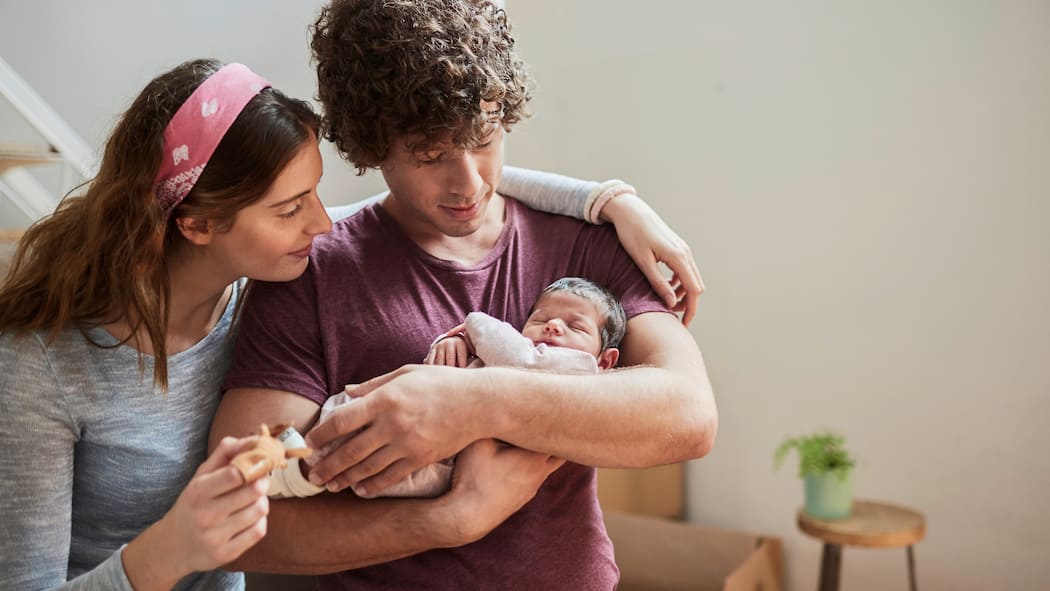 Das gemeinsame Kind absichern Ein junges Paar sieht sich ihr Neugeborenes an und sieht dabei glücklich aus.