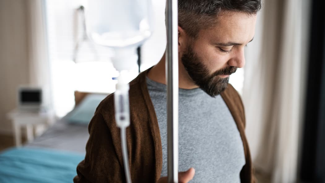Muss ich Franchise und Selbstbehalt übernehmen? Ein Patient steht in einem Spitalzimmer. In seiner rechten Hand hält er einen Ständer mit einer Infusion.