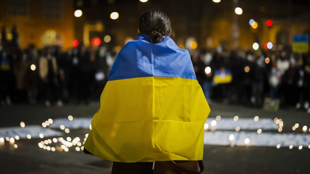 Der Beobachter hilft Eine Frau trägt eine ukrainische Flagge und spricht vor einem Meer aus Kerzen und den versammelten Demonstranten ihre Solidarität mit den Ukrainerinnen und Ukrainern aus, die vom russischen Angriffskrieg betroffen sind.