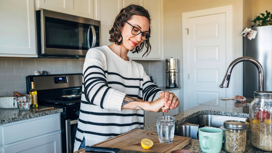 Richtig trinken – so gehts Frau presst Zitrone in Glas mit Wasser