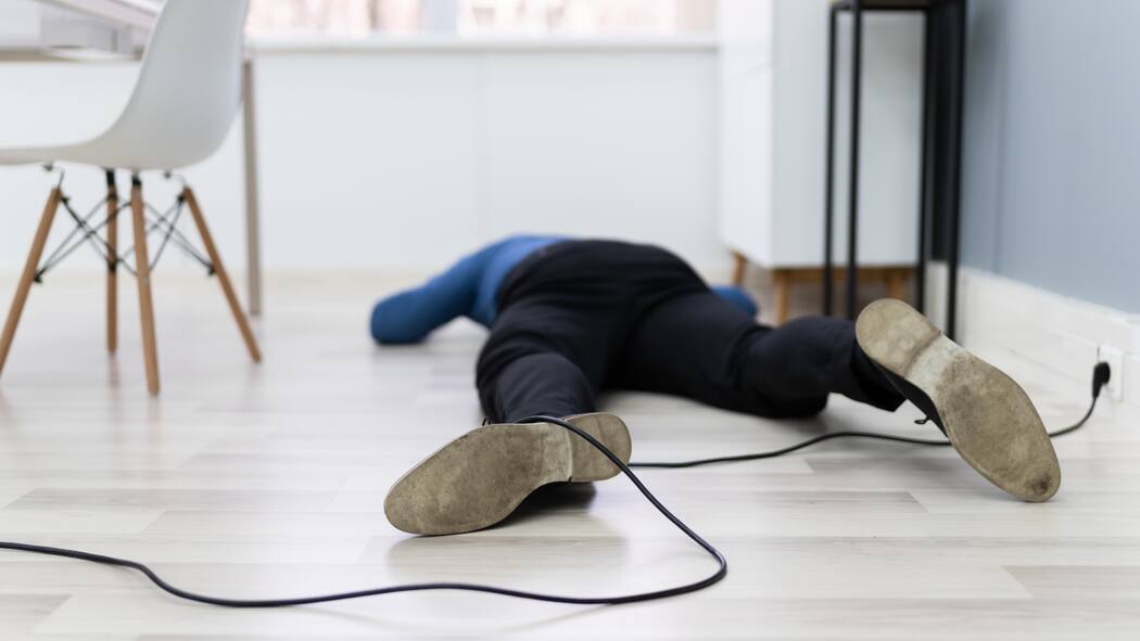 Gilt das als Berufs- oder Freizeitunfall? Ein Angestellter im Homeoffice liegt auf dem Fussboden, weil er über ein Kabel am Boden gestolpert ist.