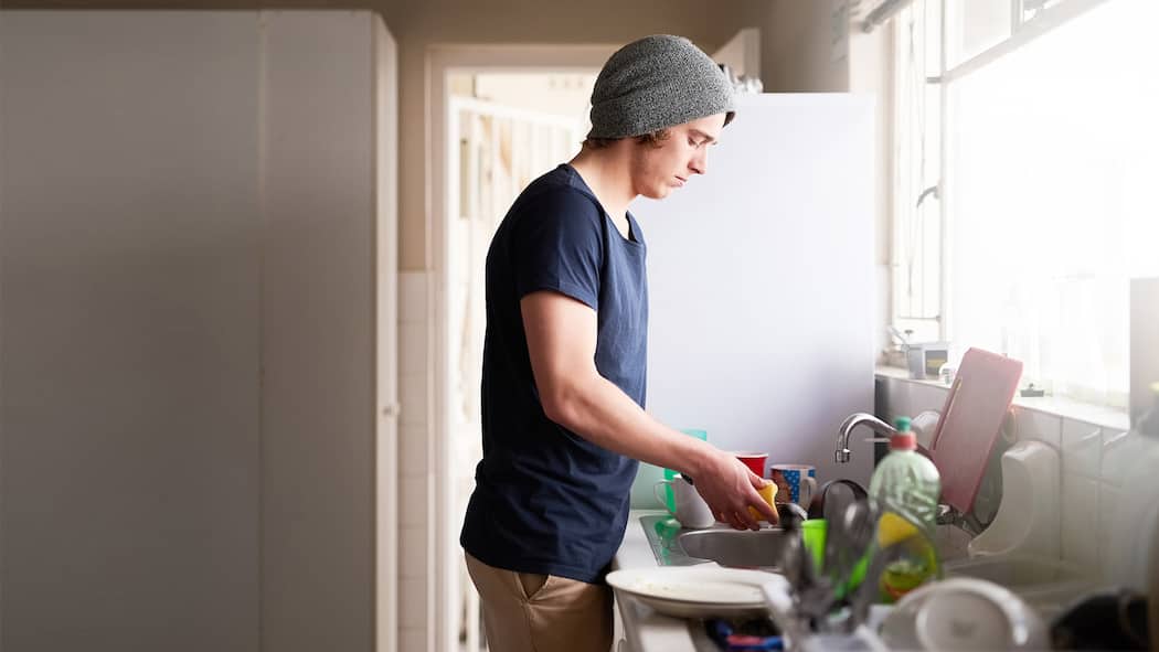 Teure Wohnung – wie viel zahlt der Staat? Ein junger Mann steht in der Küche und wäscht Geschirr ab. Günstiger Wohnraum ist für Sozialhilfebeziehende oft schwer zu finden.