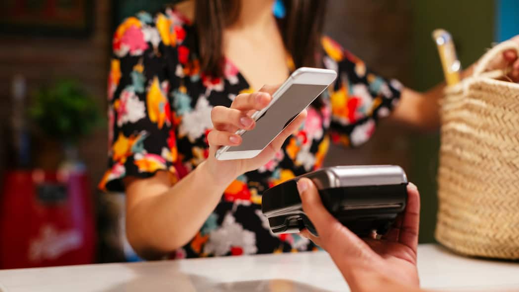 Wie steige ich auf Bargeldlos um? Eine junge Frau hält ihr Smartphone zum Bezahlen an ein Lesegerät.