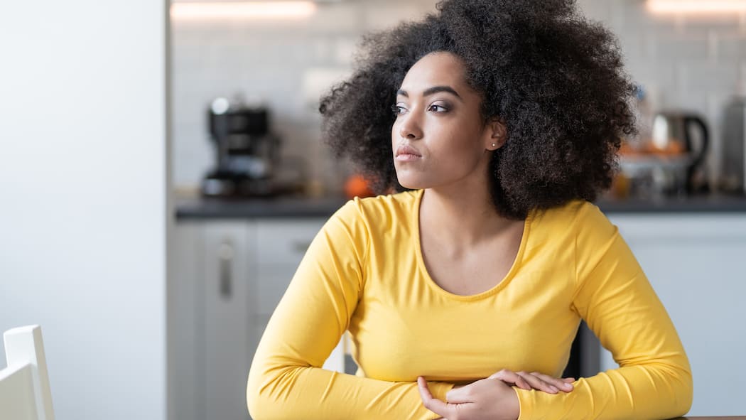 Schimmel in der Wohnung artet in Streit aus Eine junge Frau sitzt in ihrer Wohnung und schaut gedankenversunken um sich herum.