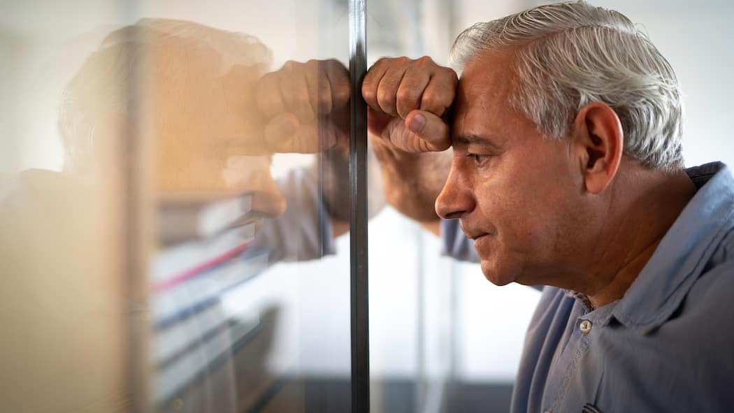 Ist das Pensionskassengeld weg? Ein besorgt dreinblickender Mann mittleren Alters lehnt sich mit der rechten Hand und seinem Kopf gegen eine Glaswand.