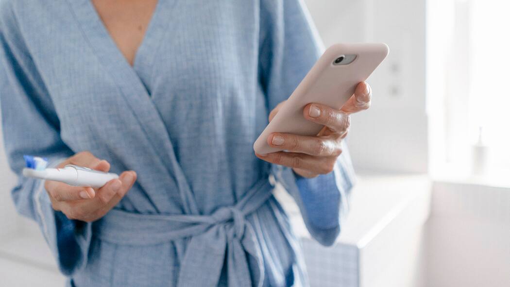 3 Tipps zur Selbstbegrenzung Eine Frau liest im Bad auf ihrem Smartphone Mails, während sie am Zähne putzen ist.