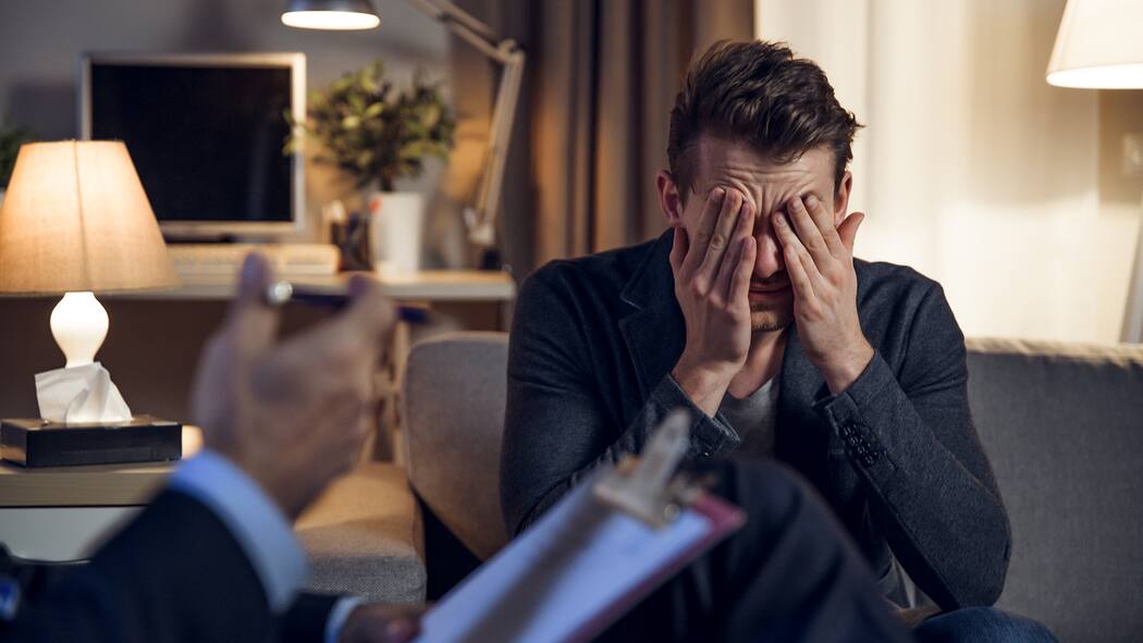 Wer kann mir durch die Krise helfen? Ein Psychotherapeut im Gespräch mit seinem Patienten, der das Gesicht in den Händen vergräbt.