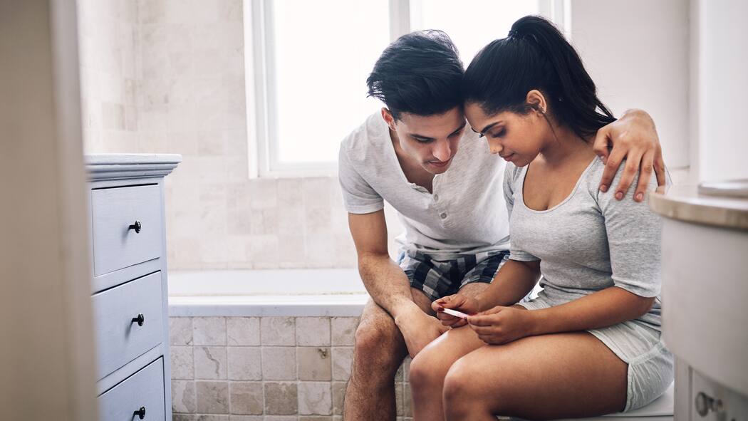 Wie viel Unterhalt zahle ich im Minimum? Ein Paar sitzt im Badezimmer und wartet auf das Resultat eines Schwangerschaftstests.