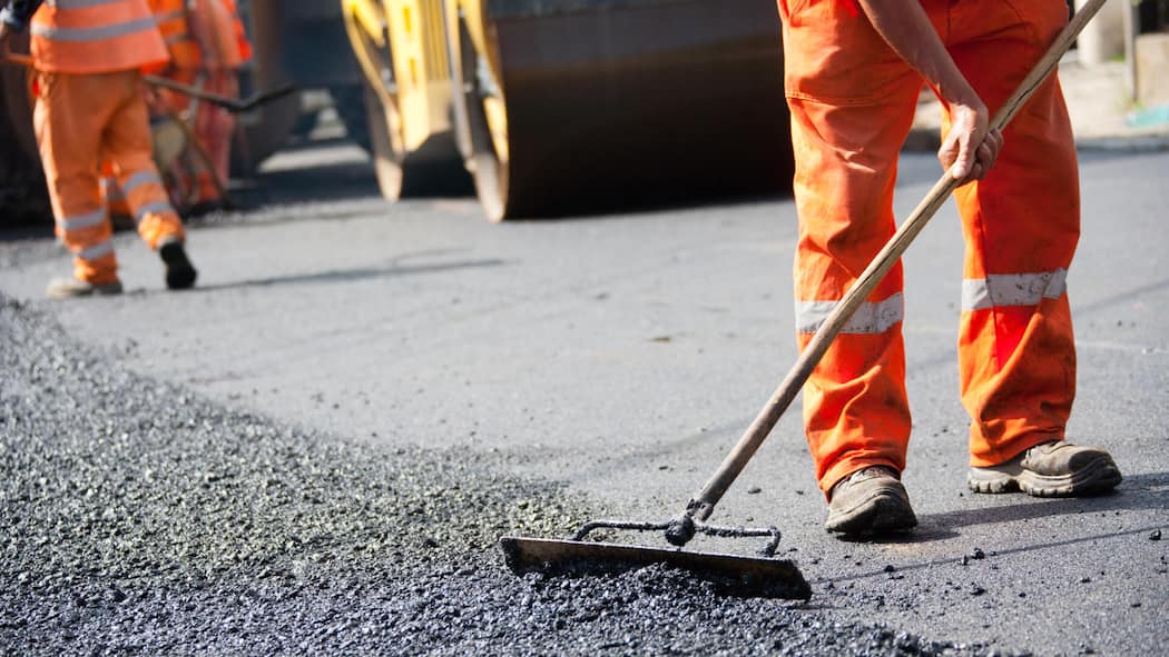 In Bern gibts eins auf die Nuss Ein Strassenbauarbeiter verteilt frischen Asphalt auf einer Strasse – Visionär und vorbildlich: Bern reguliert Lärm auf der Strasse durch Cashew-Nussschalen.