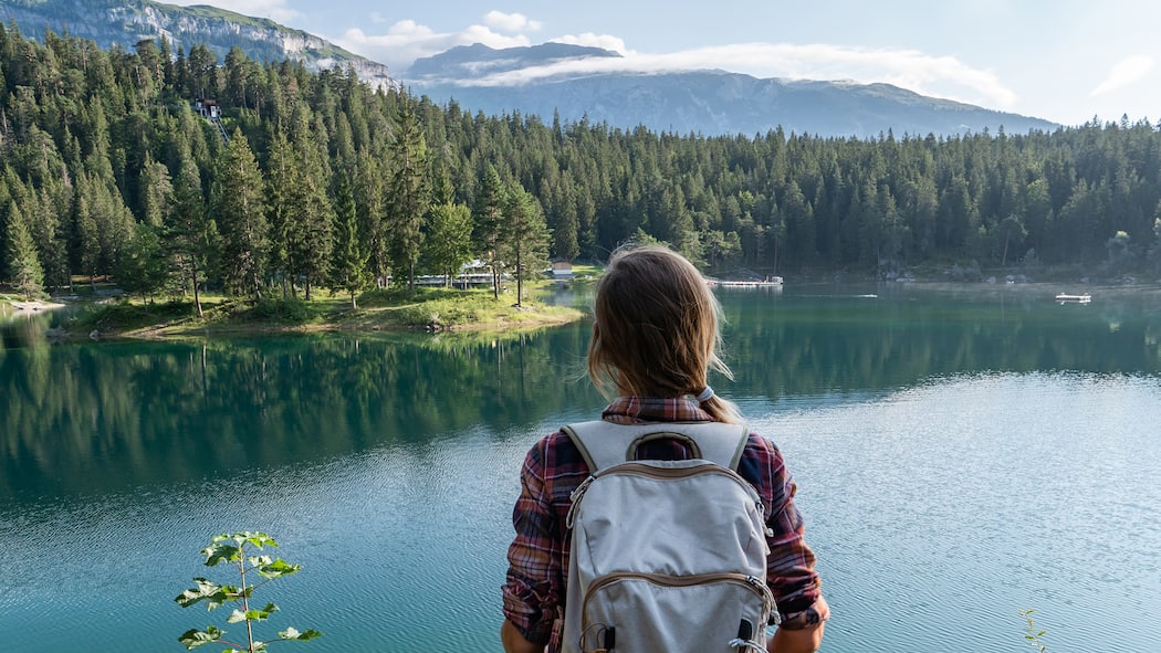 10 Tipps für nachhaltiges Reisen Junge Frau blickt auf Schweizer Bergsee und das Alpenpanorama