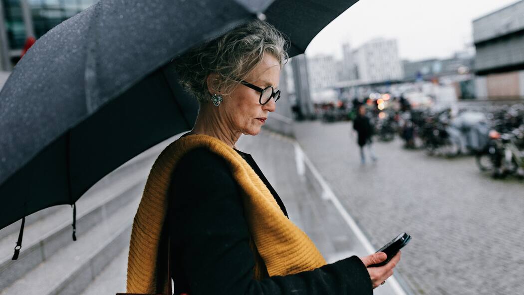6 Meteo-Apps und ihre Vorteile im Vergleich Frau steht im Regen und prüft ihr Smartphone