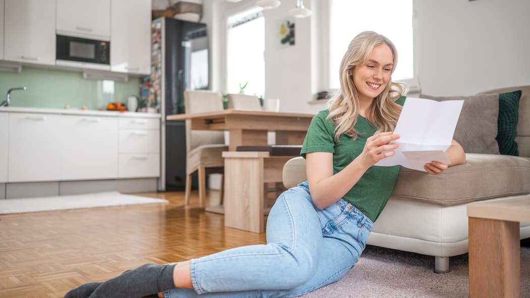 Erhalte ich die Säule 3a meines Vaters? Eine junge Frau sitzt auf dem Fussboden ihrer Wohnung und freut sich über einen Brief, den sie gerade am Lesen ist. Kann die Tochter das Guthaben aus der Säule 3a des Vaters erben, wenn dieser nichts im Testament vermerkt hat?