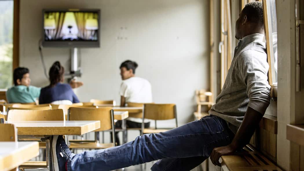 Was wird aus dem Status F? Ein Mann im Bundesasylzentrum Glaubenberg schaut hinüber zu einer anderen Gruppe Leute, die gerade fernsehen