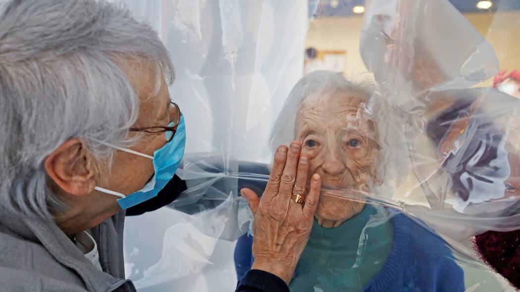 Wie schützen wir unsere Alten? Eine Frau besucht ihre 97-jährige Mutter im Altersheim, getrennt durch einen virussicheren Vorhang