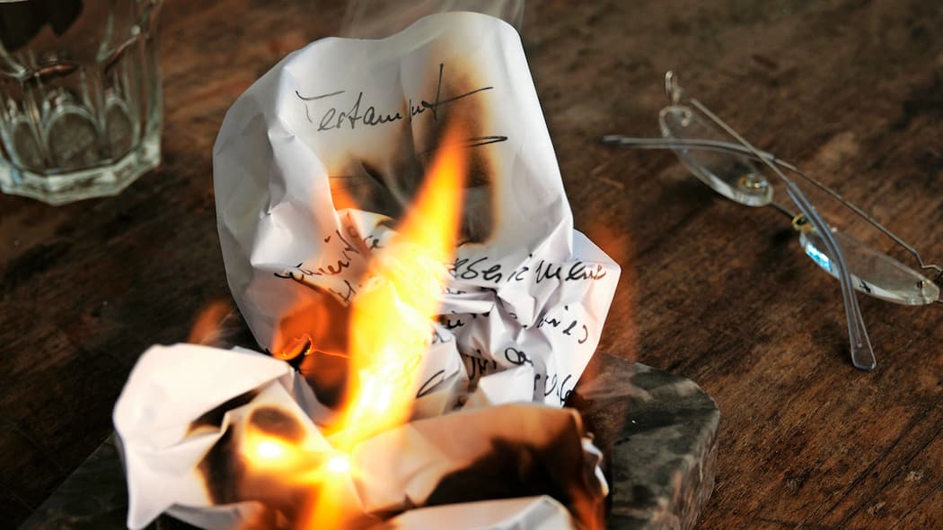 Der letzte Wille ist nicht für die Ewigkeit Ein zerknülltes Testament wird in einem Aschenbecher verbrannt, daneben liegt eine Lesebrille