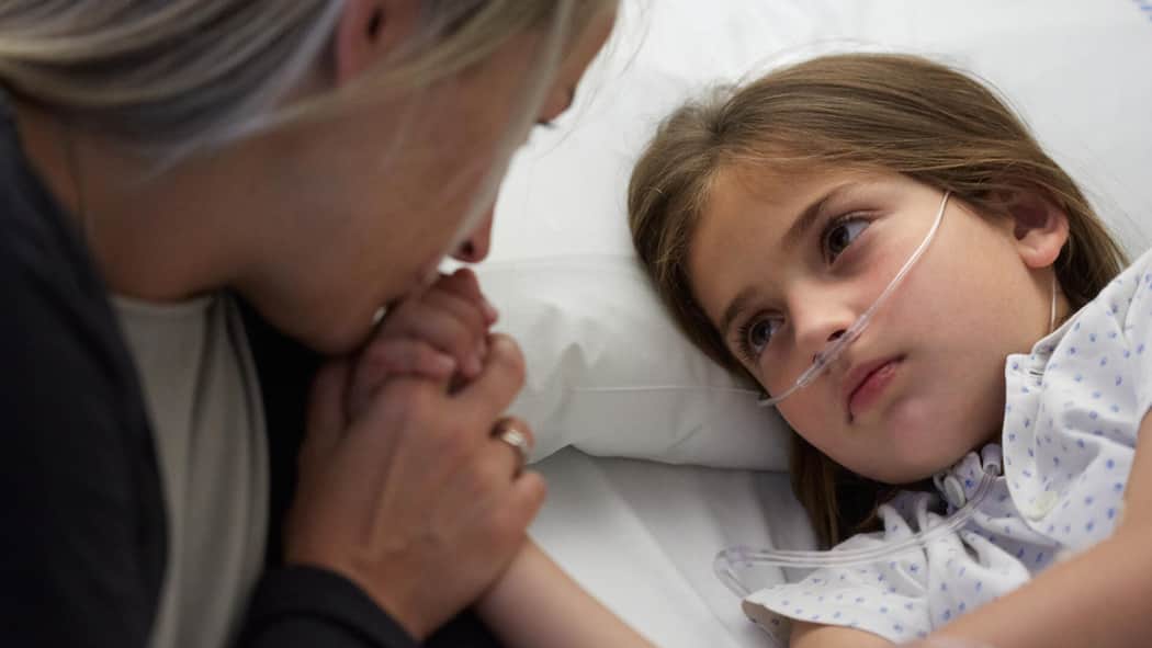 Wie lange darf ich mit meinem kranken Kind zuhause bleiben? Ein Mädchen mit Atemmaske hält die Hand ihrer Mutter. Wie die Betreuung kranker Kinder geregelt ist.