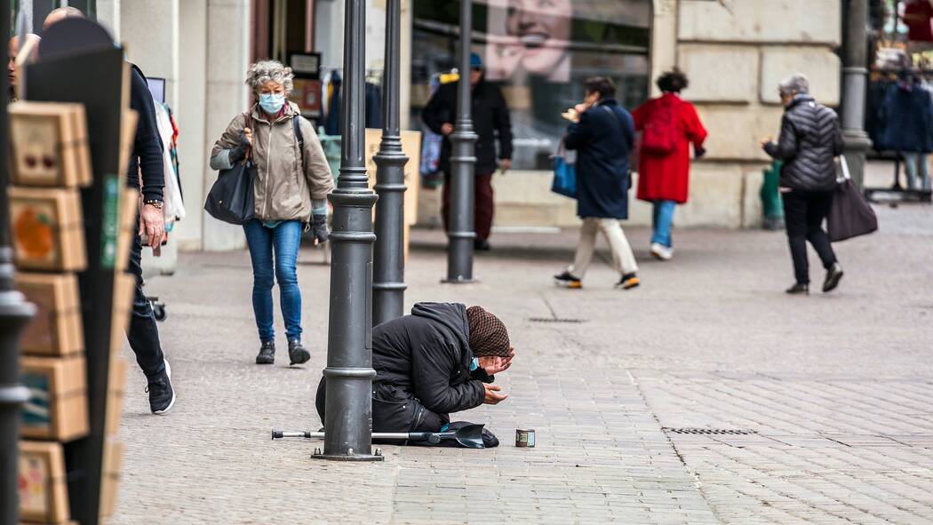 Soll ich Geld geben? Eine Bettlerin hat sich auf eine belebte Fussgängerstrasse hingekniet, ihr Blick ist nach unten gerichtet und die Menschen gehen an ihr vorbei.