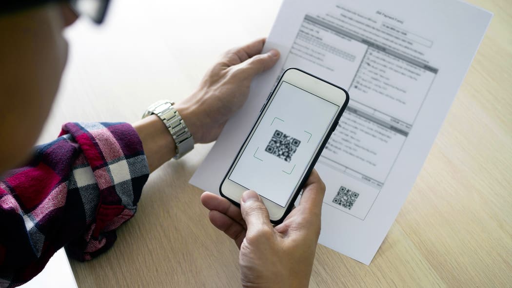 Muss ich wegen der Umstellung auf QR-Rechnung etwas tun? Ein junger Mann hat seine Handykamera auf einen QR-Code gerichtet, um diesen zu scannen.