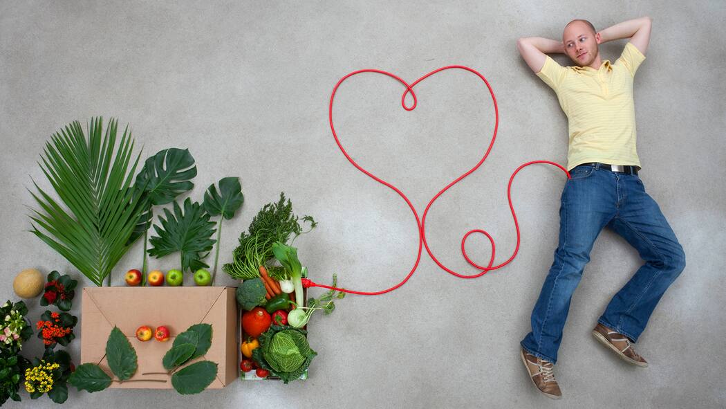 Tipps, damit das Herz nicht schlapp macht Mann liegt auf dem Boden neben ihm sind Gemüse und ein gezeichnetes Herz