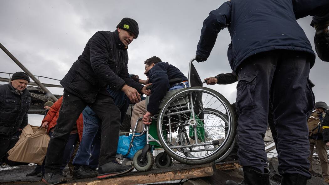Nicht für Flüchtlinge mit Behinderung eingerichtet Mann in Rollstuhl wird bei der Überquerung des Flusses in der ukrainischen Stadt Irpin geholfen
