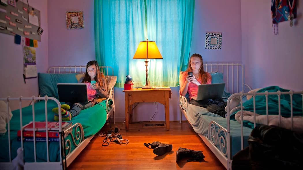 «Onlinesucht kann wirklich alle treffen» Zwei Teenager Schwestern liegen im Bett ihres Schlafzimmers. Beide haben einen Laptop auf ihren Beinen und hantieren gleichzeitig mit einem Smartphone.