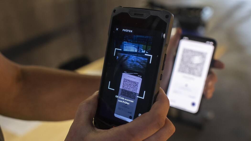 Gefälschtes Covid-Zertifikat – welche Strafe droht? Mann kontrolliert mit Smartphone Covid-Impfzertifikat