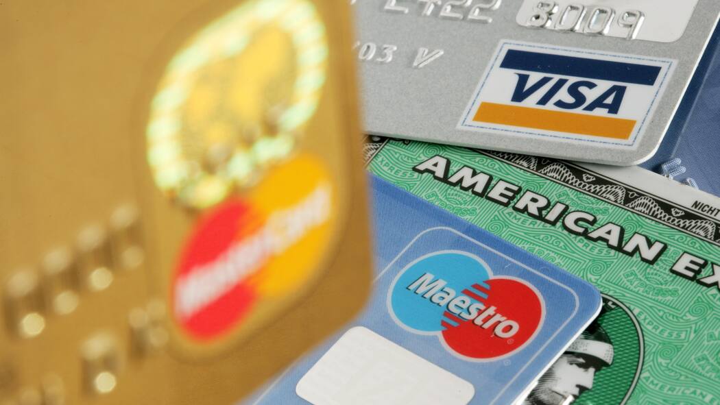 Warum soll ich eine teurere Bankkarte akzeptieren? Auf einem Tisch liegen verschiedene Bankkarten: Maestro, Visa, Mastercard und American Express