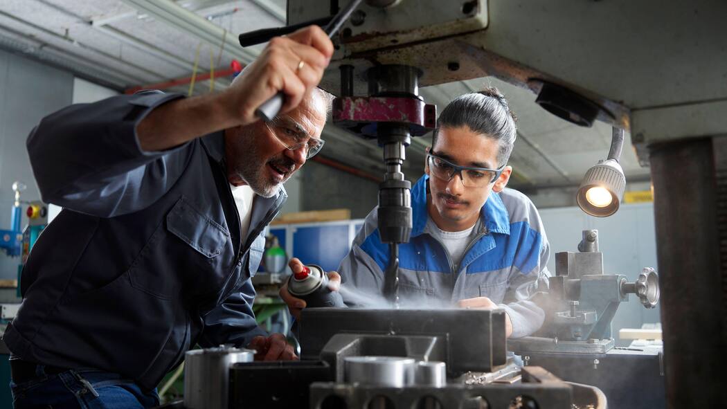 Neue Ansätze sollen jungen IV-Bezügern helfen 2T97J4G Instructor with trainee spraying lubricant on drill bit at workshop