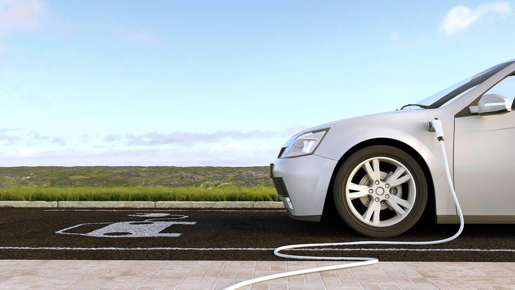 Ladestation vor der Haustür Ein E-Auto steht im Freien auf einem Parkplatz und wird durch ein am Boden verlegtes Ladekabel aufgeladen.