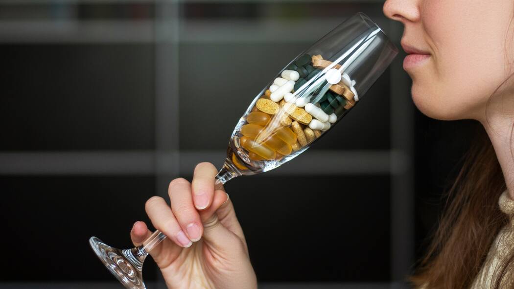 Ein riskanter Cocktail Eine Frau trinkt aus einem Champagnerglas, das mit Medikamenten gefüllt ist.