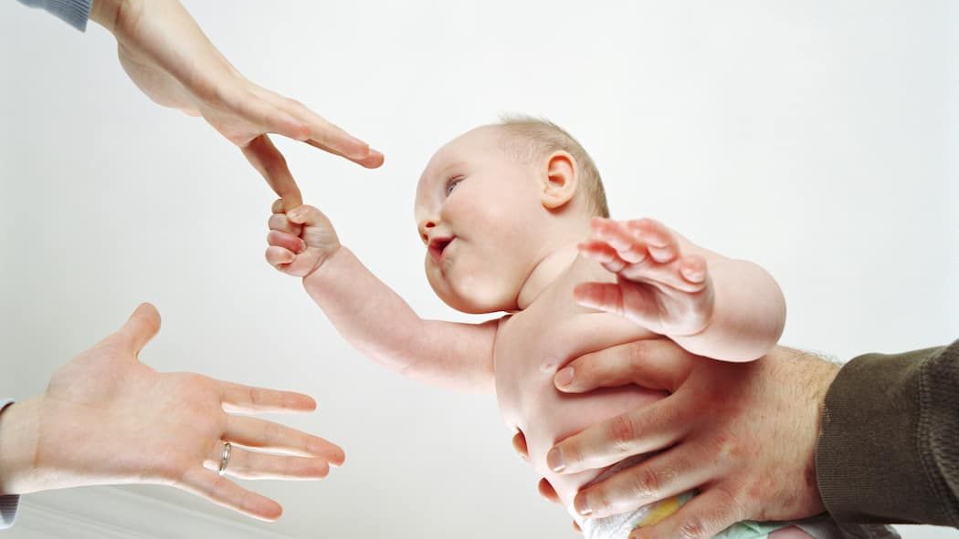 «Elternsein ist nicht schwieriger als früher. Nur anders» Zwei Paar Hände greifen nach Baby. Maternal Gatekeeping, Mental Load und Erschöpfung - Ein Gespräch mit Psychologin Valentina Rauch-Anderegg über die Tücken des modernen, gleichberechtigten Elternlebens.