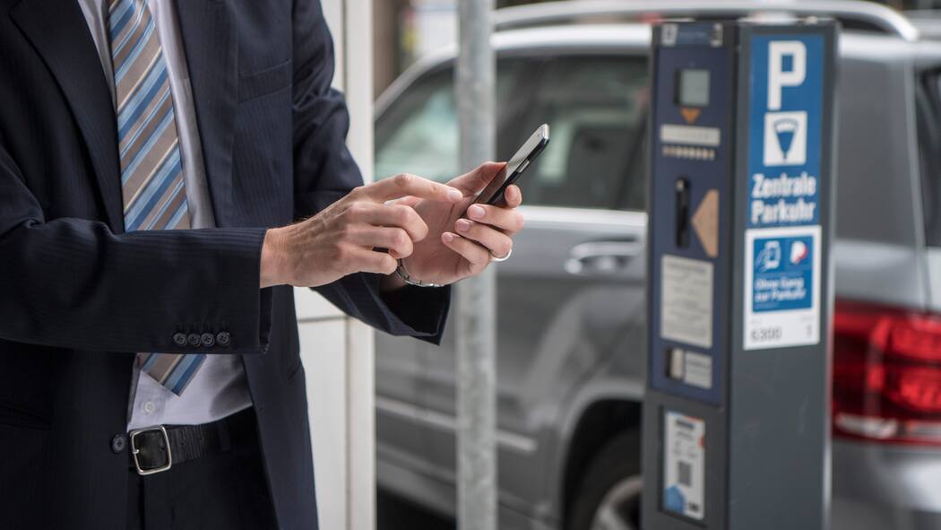 85 statt 5 Franken bezahlt – Polizei bleibt streng Zu sehen ist ein Mann im Anzug, der gerade etwas auf seinem Handy eintippt. Er befindet sich direkt neben einer Säule für das Bezahlen von Parkgebühren.