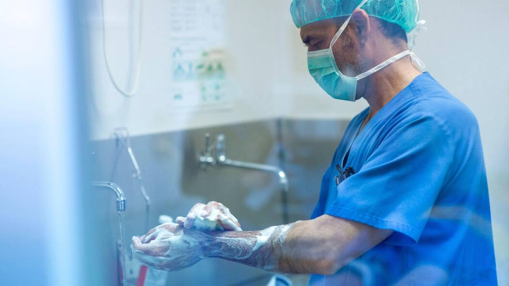 5900 Tote jährlich durch Infektionen im Spital 2E4JEPP Male surgeon in surgical cap using smart phone at hospital