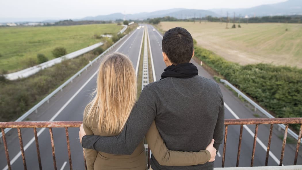«Wie können wir unsere Situation verbessern?» Ein Paar steht auf einer Autobahnüberführung, der Blick auf die weite Strasse gerichtet und hält sich dabei in den Armen.