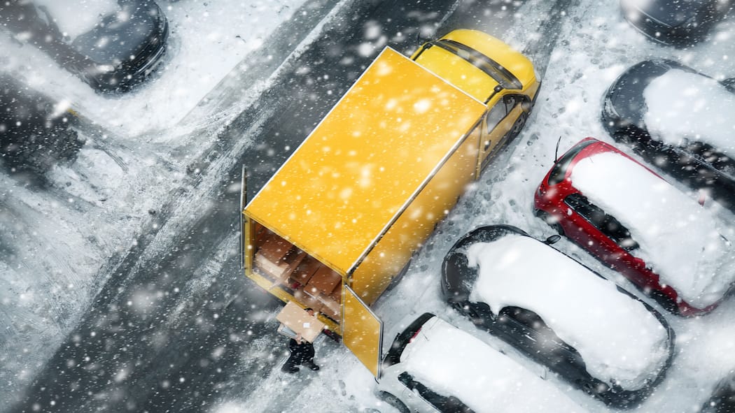 Das lange Warten aufs Geschenk Ein gelber Lieferwagen steht auf einem verschneiten Parkplatz zwischen anderen Autos.