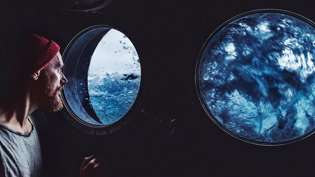 Tipps gegen Reiseübelkeit Ein seekranker Mann schaut aus dem Bullauge eines Schiffs auf den Wellengang des Meeres.