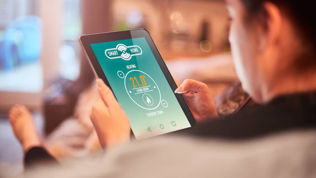 Kontrollieren Sie die Temperatur im Feriendomizil per App Homeowner using Smart home heating technology on the sofa in living room of modern home