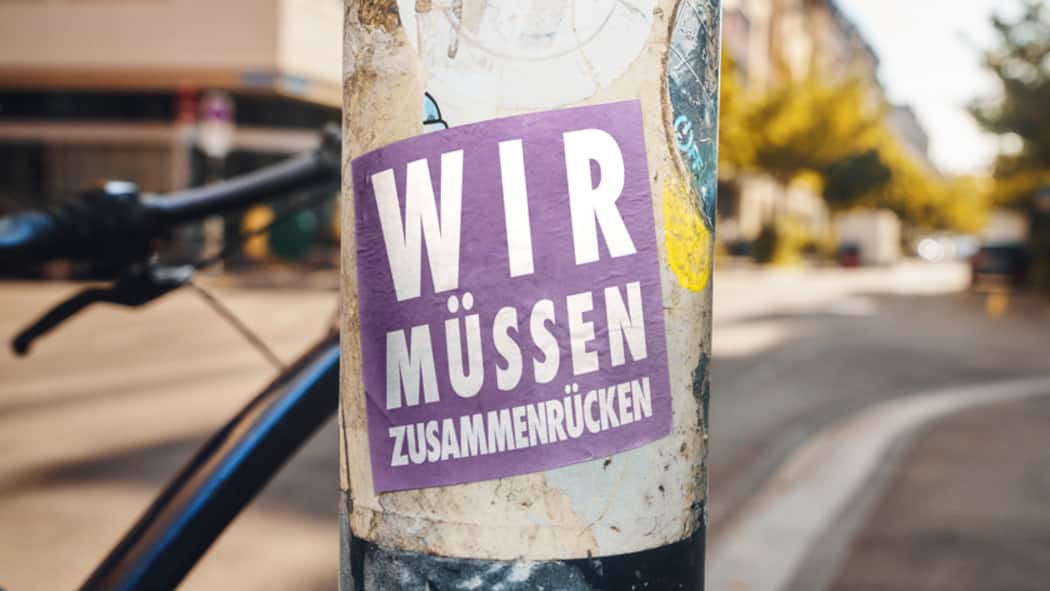 Wir werden immer mehr – was heisst das? Sticker mit Aufschrift: Wir müssen zusammenrücken