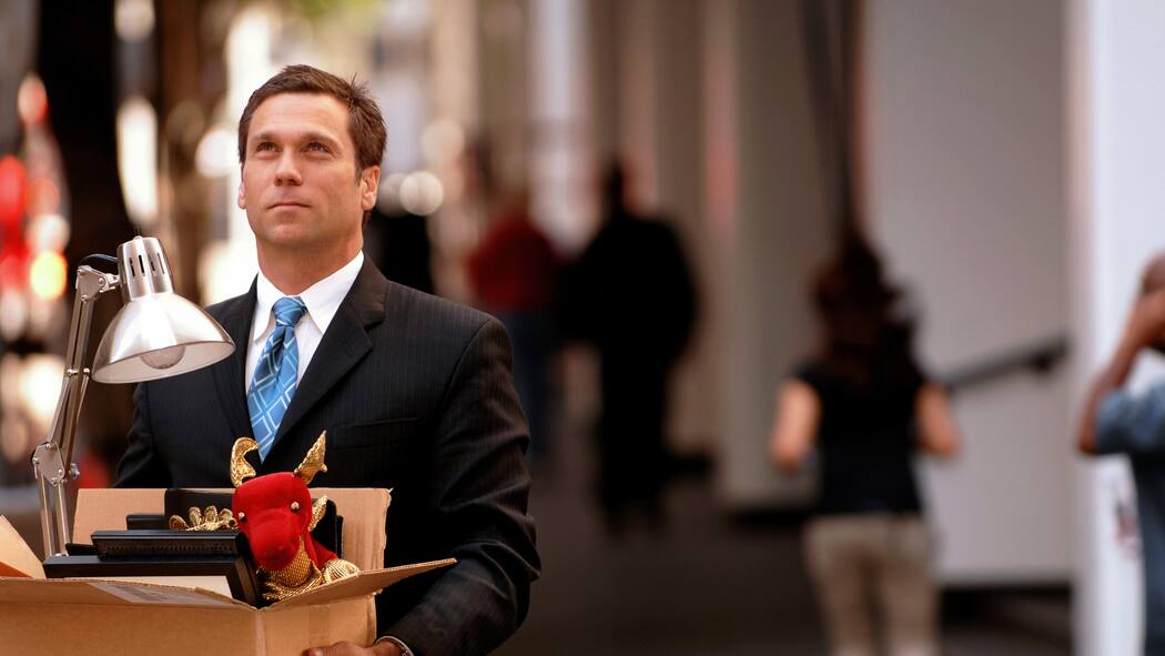 Das sind die Regeln bei Entlassung Geschäftsmann im Anzug hält eine Kartonschachtel mit persönlichen Gegenständen seines Arbeitsplatzes in der Hand und verlässt die Geschäftsräume.