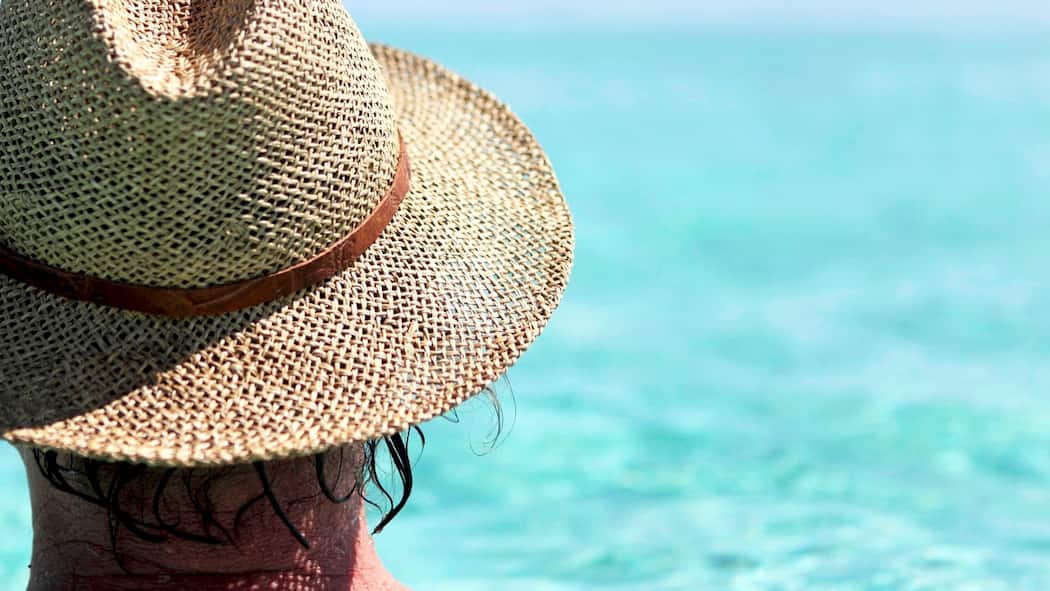 Vor diesen Reisekrankheiten sollten Sie sich schützen Mann mit Sonnenhut blickt aufs offene Meer