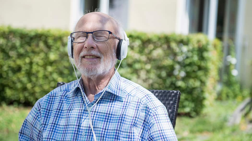 Heilsame Töne Ein älterer Mann sitzt im Garten und hört Musik.