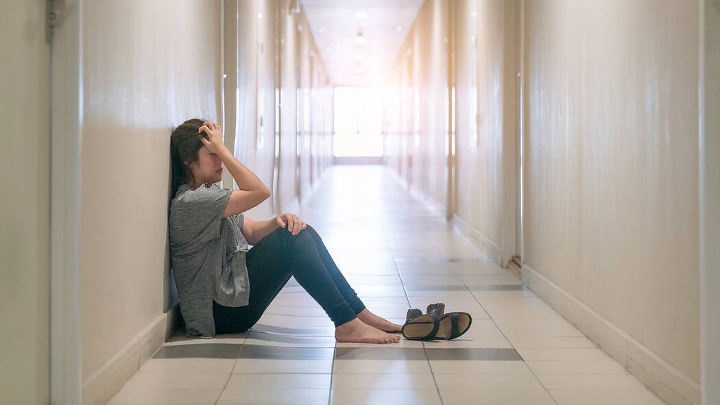 Wie können Angehörige damit umgehen? Eine Frau sitzt in einer Klinik auf dem Boden und schlägt die Hände vors Gesicht.