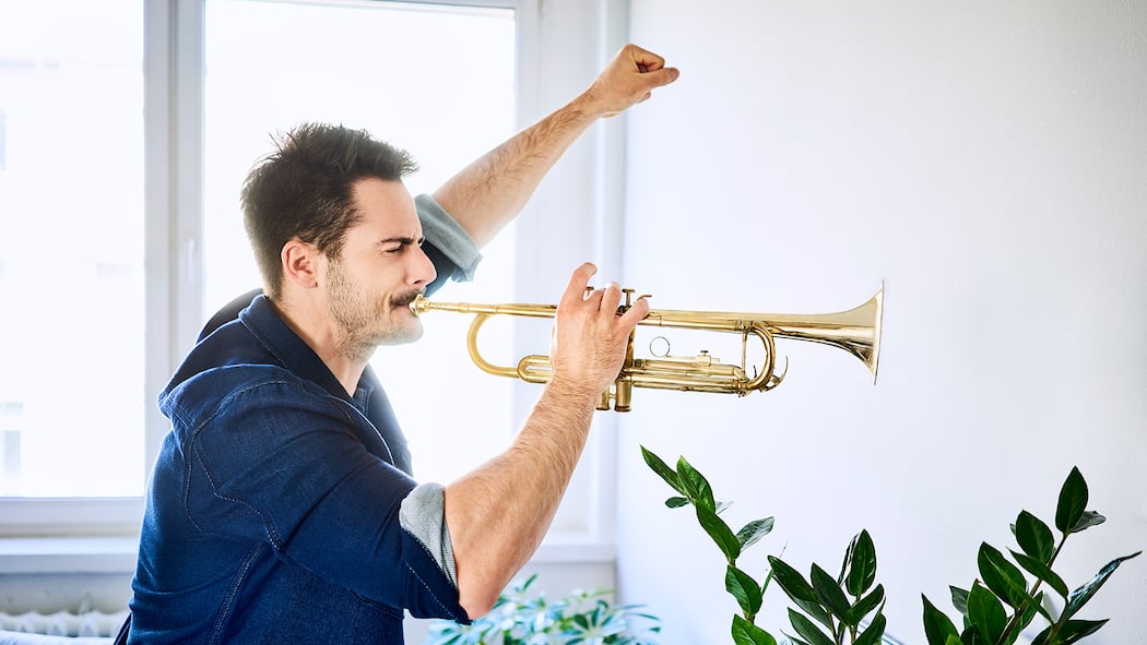 Wer will Krach? Ein junger Mann spielt mit erhobener Faust Trompete in der Wohnung
