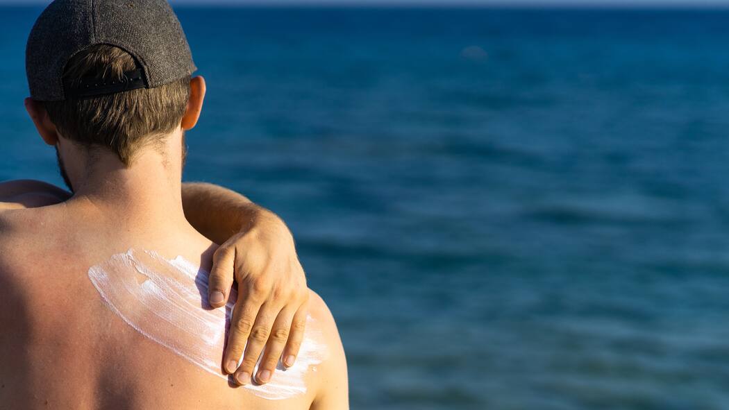 Chemische und natürliche Sonnencremes im Vergleich Mann cremt sich am Strand mit Sonnencreme ein