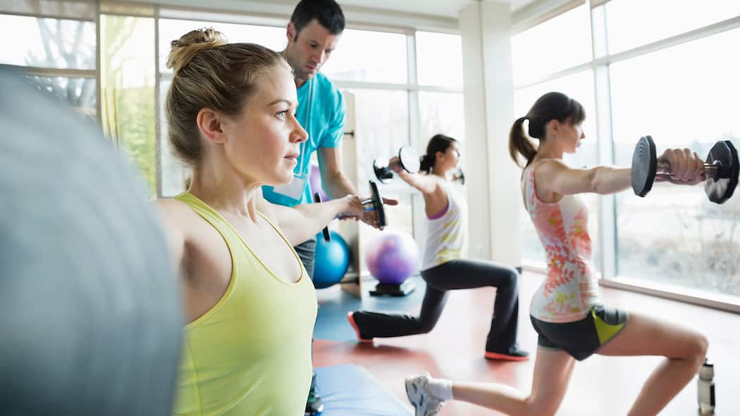 Muskeln ohne Katerstimmung Eine Frau trainiert mit einer Hantel und der Trainer gibt Anweisungen.
