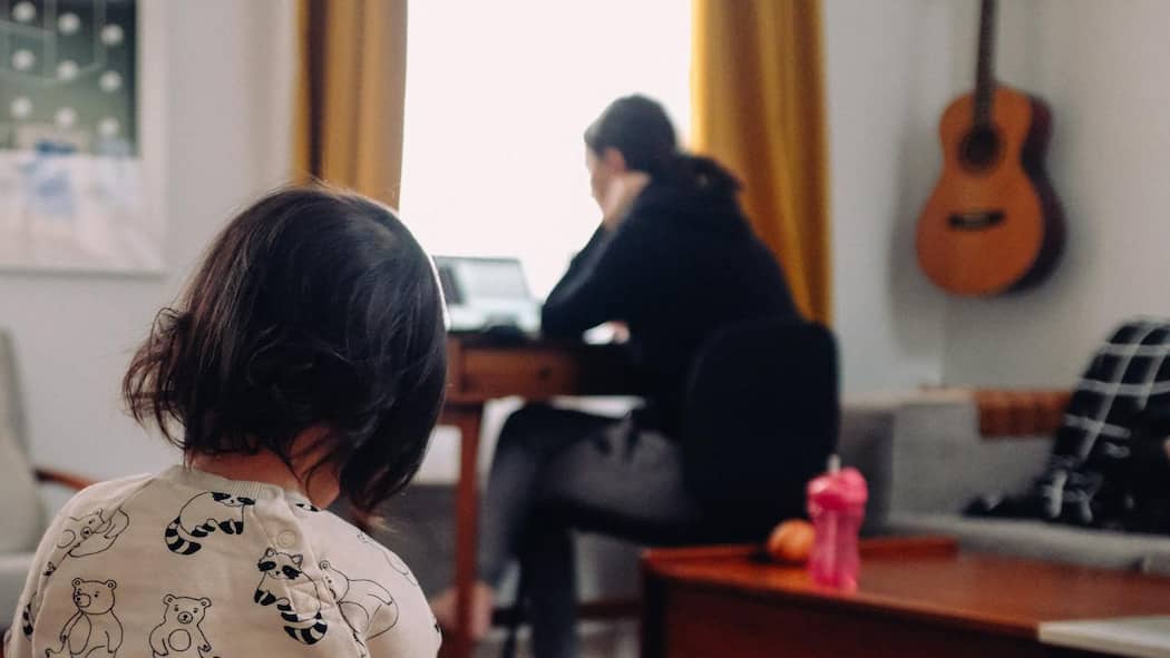 Quarantäne im Arbeitsverhältnis Eine Frau sitzt vor dem Laptop während das Kind in der Wohnung spielt