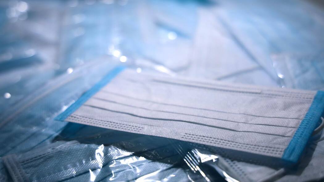 Maskenpflicht im Arbeitsverhältnis Dutzende Schutzmasken liegen ausgebreitet auf einer Oberfläche