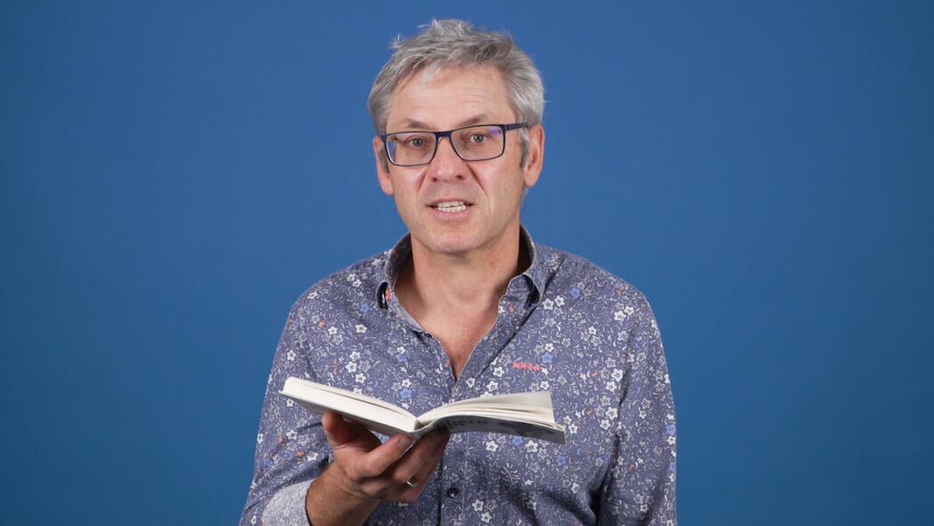 Wie funktioniert ein Passwort-Manager? Beobachter-Redaktor Thomas Angeli sitzt vor einem blauen Hintergrund und hält ein Buch in seiner rechten Hand.