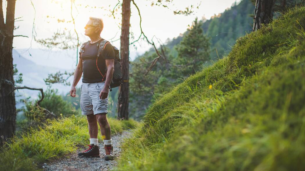 Wie die Sinne die Selbstheilung unterstützen Ein Mann blickt auf einer Wanderung nachdenklich in die Landschaft
